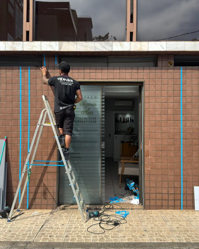 Instalador da DPrint na escada aplicando material na fachada de uma loja